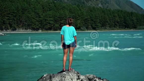 年轻女子站在快速山河旁的一件蓝色t恤上看着江流背面视频的预览图