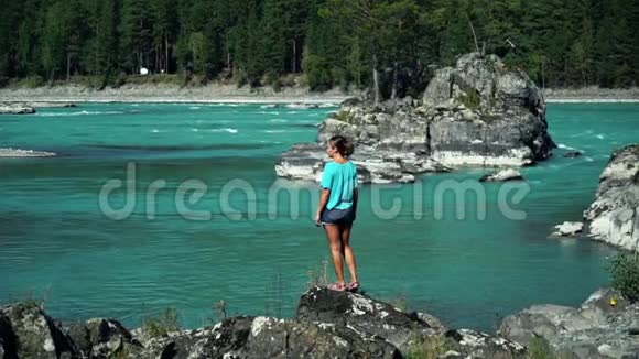 穿着蓝色t恤的年轻女子站在纯净的山河旁看着江流背面视频的预览图