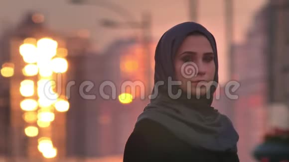 年轻迷人的穆斯林妇女戴着头巾在镜头前带着忧郁的微笑在城市里闪闪发光视频的预览图