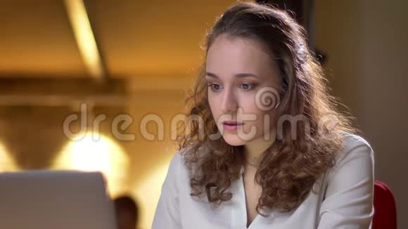 年轻的卷发女子的特写肖像非常高兴并在办公室亲吻笔记本电脑视频的预览图