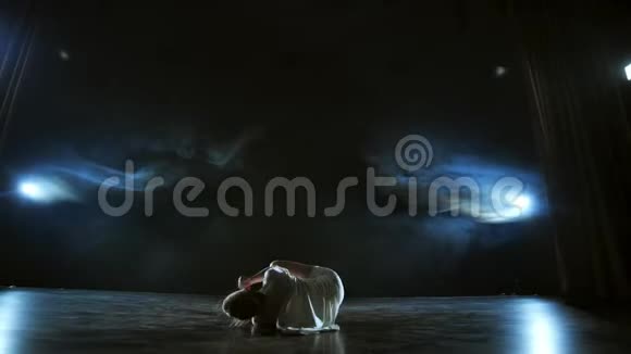 现代舞女穿着白色连衣裙跳着现代芭蕾在舞台上用蓝色的烟雾旋转视频的预览图