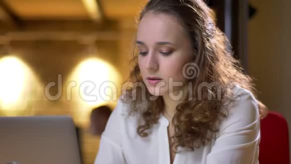 一位年轻的卷发女士的特写肖像她专心地用笔记本电脑工作在办公室里愉快地喝着饮料视频的预览图