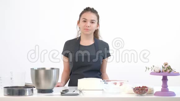 漂亮的黑发女孩糕点厨师在围裙鞭打奶油蛋糕在一个金属碗视频的预览图