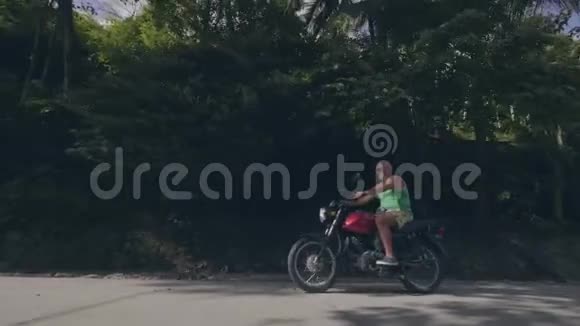 在热带棕榈树景观的乡村道路上骑摩托车的老年摩托车司机骑马的长者视频的预览图