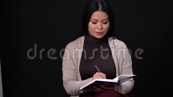 专注的亚洲女人在笔记本上写字视频的预览图