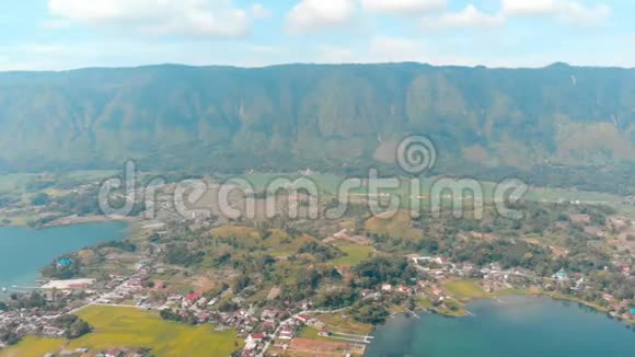 空中来自印度尼西亚苏门答腊岛上方的托巴湖和萨莫西尔岛巨大的火山岩覆盖着水巴塔克村绿色的视频的预览图