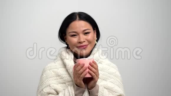 戴着白色围巾的美丽亚洲女人端着一杯茶视频的预览图
