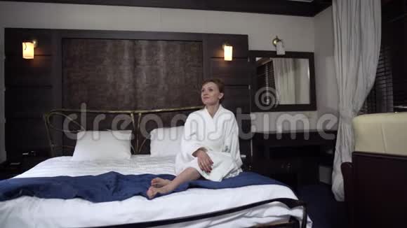 一对情侣穿着白色浴袍坐在宽大的床上喝着酒杯里的红酒家庭休闲视频的预览图
