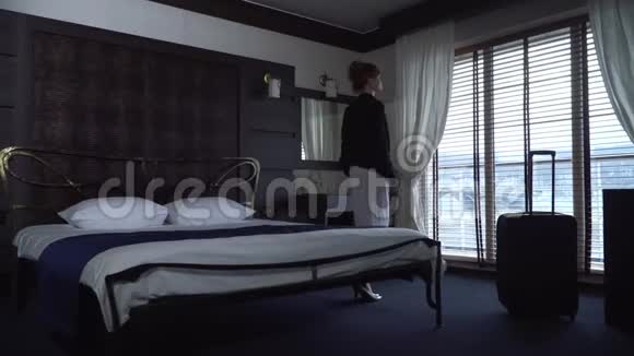 在一家舒适的小旅馆里一个年轻疲惫的女人坐在一张漂亮的宽床上对面是落地窗和百叶窗视频的预览图