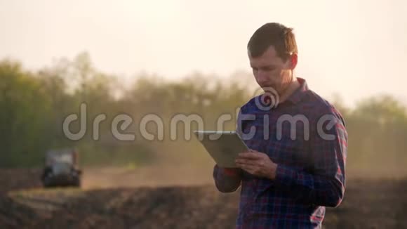 一位年轻的农艺师在田里工作用的是平板电脑在背景中拖拉机失去了焦点农民视频的预览图