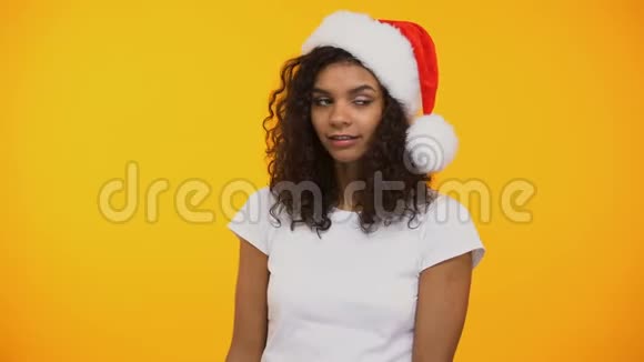 可爱的卷发女孩戴着圣诞帽手里拿着红色的新年礼物盒显得很安静视频的预览图