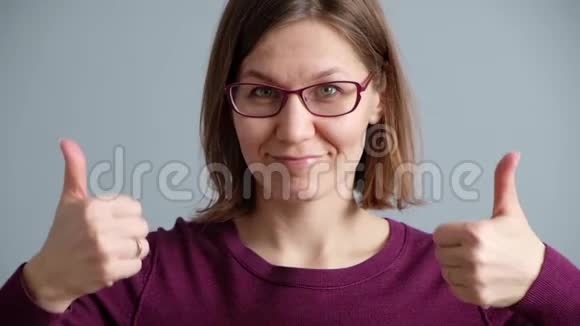 微笑的幸福女人竖起大拇指在灰色背景下看着镜头视频的预览图