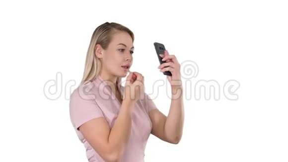 美女人化妆年轻的女人嘴唇看着白色背景上的智能手机视频的预览图