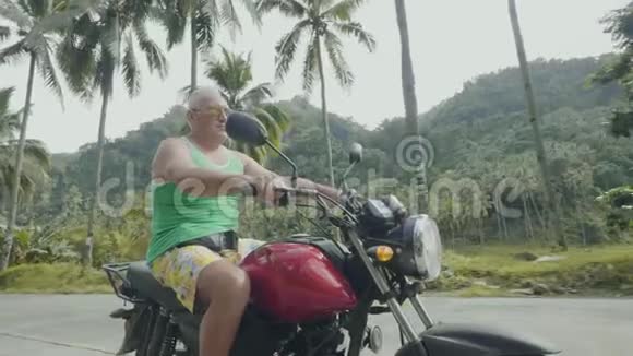 英俊的男子摩托车骑摩托车在道路上的热带棕榈树背景一位老人在旅行视频的预览图