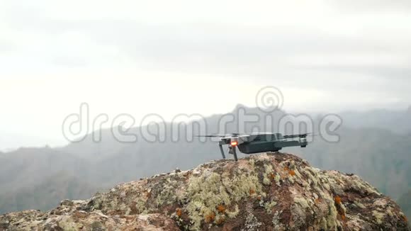 关闭一个消费无人机发射和起飞从一个粗糙的岩石高山慢动作地面视频的预览图