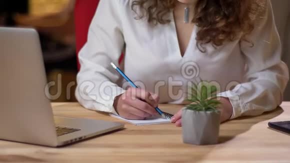 年轻卷发女子的特写肖像专心致志地写在笔记本上微笑着在办公室拍摄视频的预览图