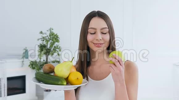 一位美丽的年轻女子在白色背景上摆着一盘水果的肖像视频的预览图