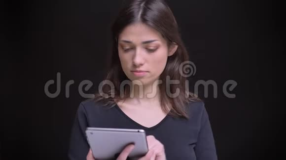 一个长着长发的黑发女孩盯着平板电脑微笑着用黑色镜头把它那直立的绿色屏幕显示出来视频的预览图
