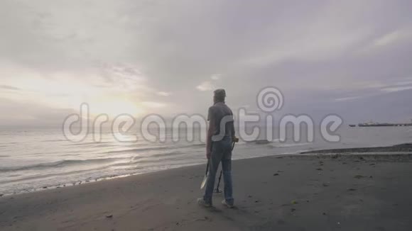 中年男子寻宝者戴着金属探测器的耳机在日落时在海洋沙滩上工作视频的预览图
