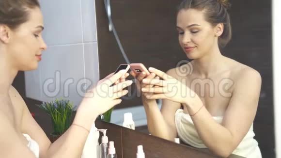 微笑的女人在浴室镜子的手机上拍照视频的预览图