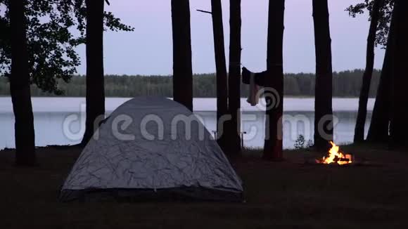 黄昏时湖边露营地的景色帐篷和火烧的地方被水包围在森林里的树木开支视频的预览图