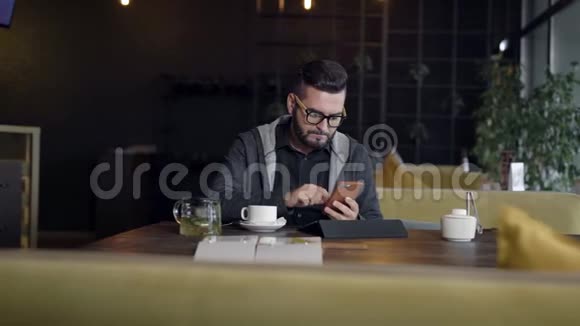 帅哥白天坐在餐厅里用智能手机在屏幕上打字平板电脑在前面视频的预览图