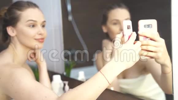 微笑的女人在浴室镜子的手机上拍照视频的预览图