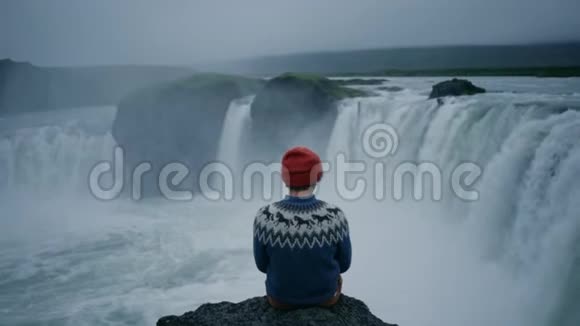 穿羊毛衫的人在瀑布岩边视频的预览图