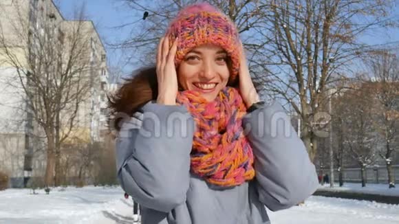 美丽的成年女孩穿着温暖的外套戴着五颜六色的针织帽子和围巾在阳光明媚的春天在户外玩视频的预览图