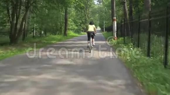 女孩骑自行车沿着柏油路穿过绿树视频的预览图