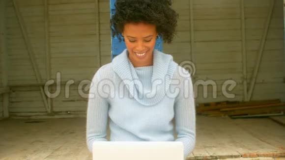 年轻的非洲裔美国妇女坐在沙滩小屋里用笔记本电脑视频的预览图