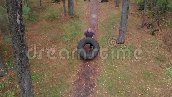 一个纹身的强壮的健美男子推着轮胎在森林的地面上视频的预览图