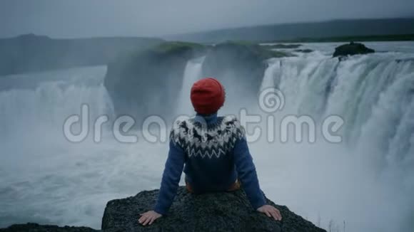 穿羊毛衫的人在瀑布岩边视频的预览图