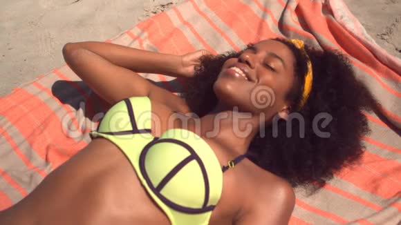 美丽的年轻非洲裔美国妇女穿着绿色比基尼在海滩的毯子上放松视频的预览图