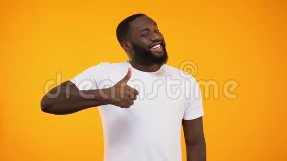 年轻的大胡子黑人竖起大拇指对着黄色背景的摄像机微笑视频的预览图