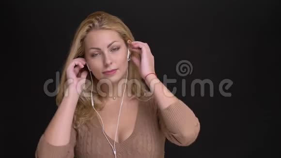 一幅快乐的白种人长发女子戴着耳机在黑色背景下欢快地随着音乐起舞的肖像视频的预览图