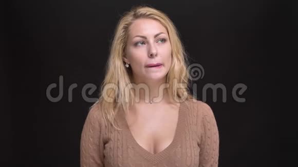 美丽的白种人长发女人在黑色背景上体贴地咬着嘴唇的肖像视频的预览图
