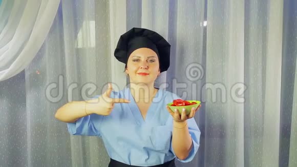 女人穿着围裙做饭微笑手里拿着樱桃番茄在盘子里用她的手展示视频的预览图