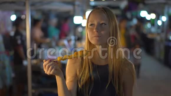 在亚洲的一个夜市上一位正在吃烤肉的年轻美女的特写镜头发出尖叫声旅游亚洲概念视频的预览图
