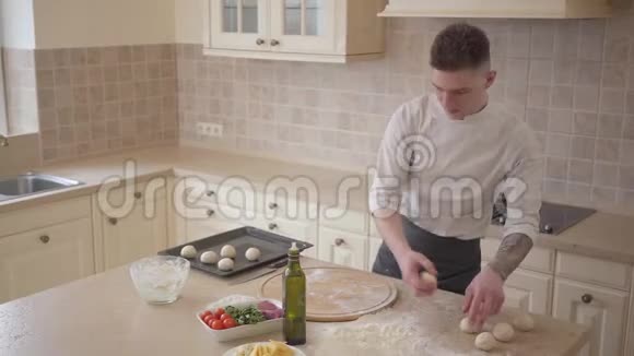 年轻的比萨饼师穿着厨师制服把面团球放在厨房的烤盘上食品准备概念视频的预览图