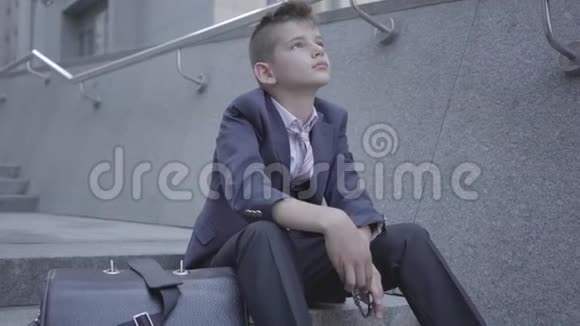 悲伤的衣冠楚楚的男孩坐在街上的楼梯上这个男孩很累想做个孩子作为儿童视频的预览图