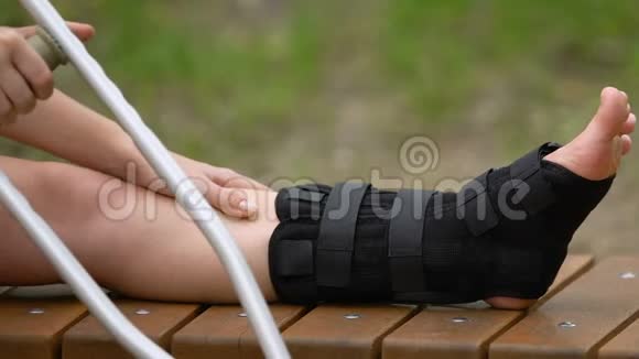 拄拐的女性患者在户外活动时用手扶按摩疼痛的腿部视频的预览图