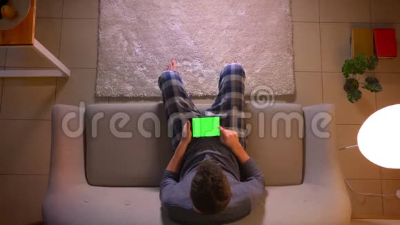 一个年轻人坐在室内的沙发上看着一则广告平板电脑上有绿色屏幕视频的预览图