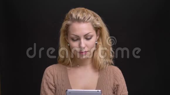 一幅美丽的白种人长发女子的肖像欢快地将绿色的平板电脑屏幕显示在黑色相机上视频的预览图