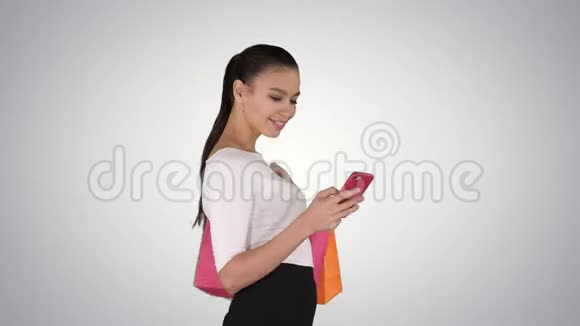 漂亮的年轻女人用手机走路拿着购物袋在梯度背景下视频的预览图