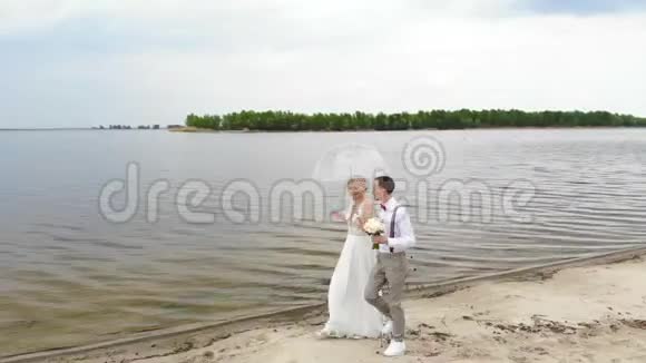 空中美丽的新婚夫妇沿着海滩散步在一把透明的伞下对着蓝天河流和一个视频的预览图