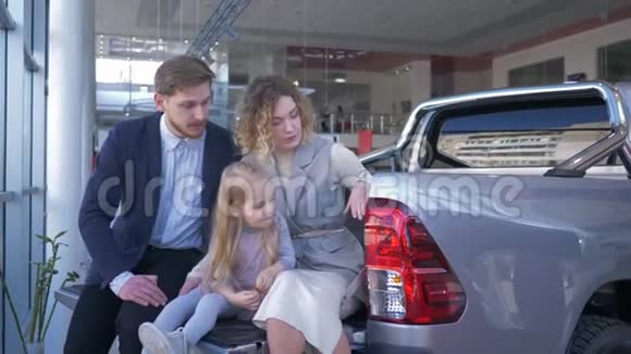汽车店女儿幸福家庭的画像选择汽车坐在后备箱里互相咨询视频的预览图