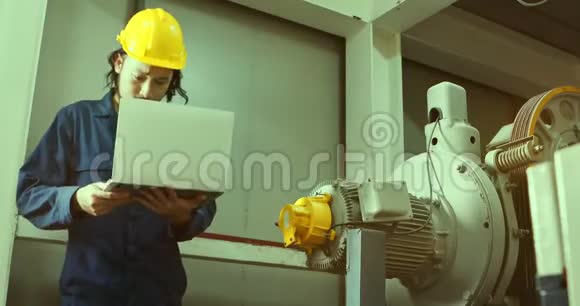 年轻的亚洲工程师在工厂的重型机械附近使用笔记本视频的预览图