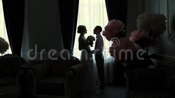 窗户对面新娘和新郎的黑暗轮廓女孩和年轻人站在一边面对着每一个人视频的预览图