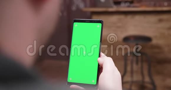 肩膀上手持镜头的男子看着手机与绿色屏幕视频的预览图